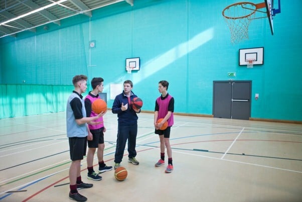 Indoor sports facilities with a coach and young players training on an indoor basketball court.